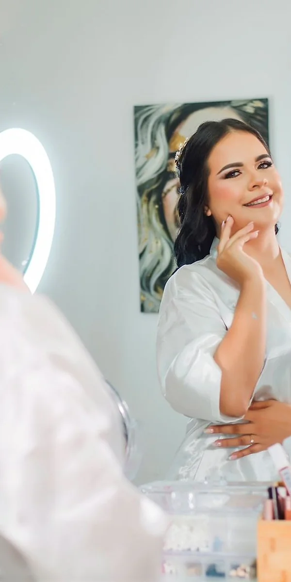 Novia sonriente mirándose al espejo durante preparación — sesión Alejandra Suárez Makeup Artist