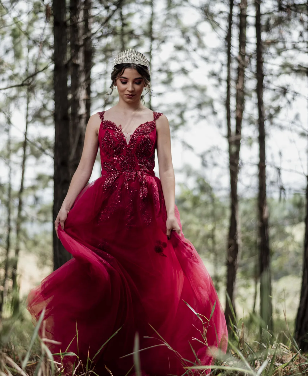 Quinceañera con vestido rojo y tiara en bosque