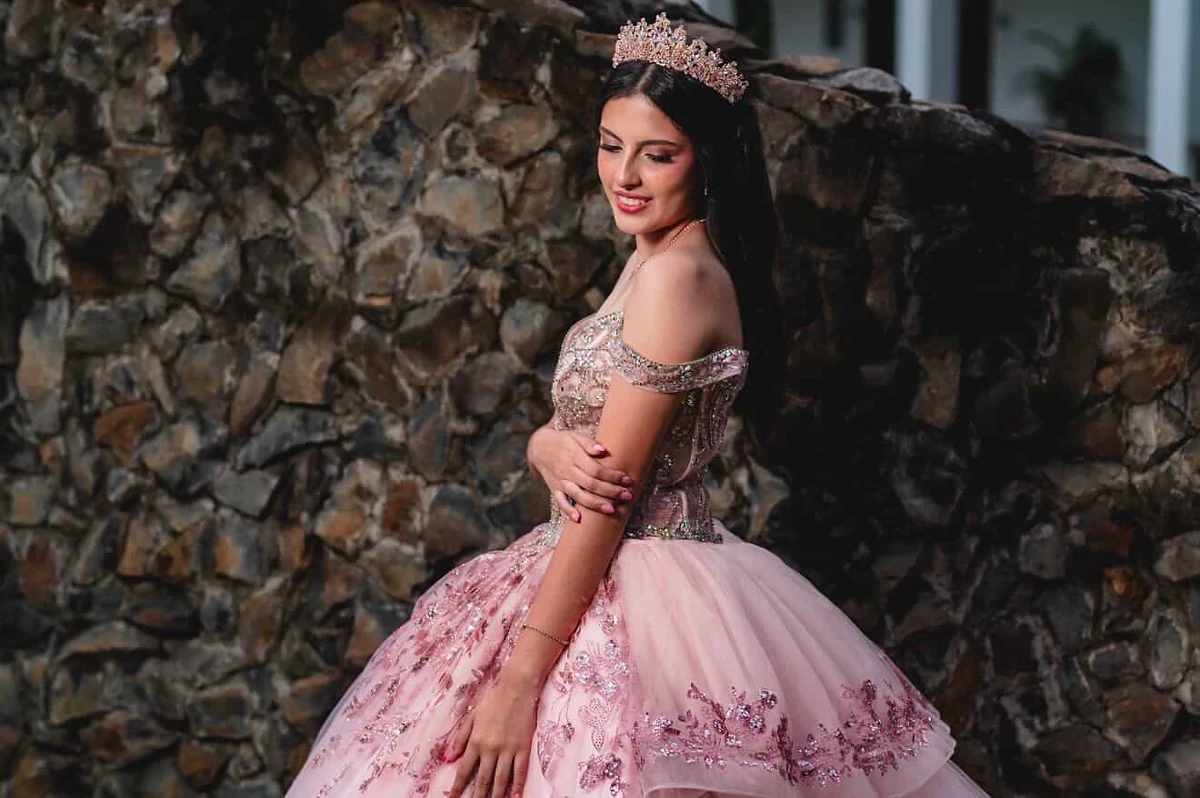 Quinceañera con vestido rosa de cristales y corona — sesión editorial con muro de piedra
