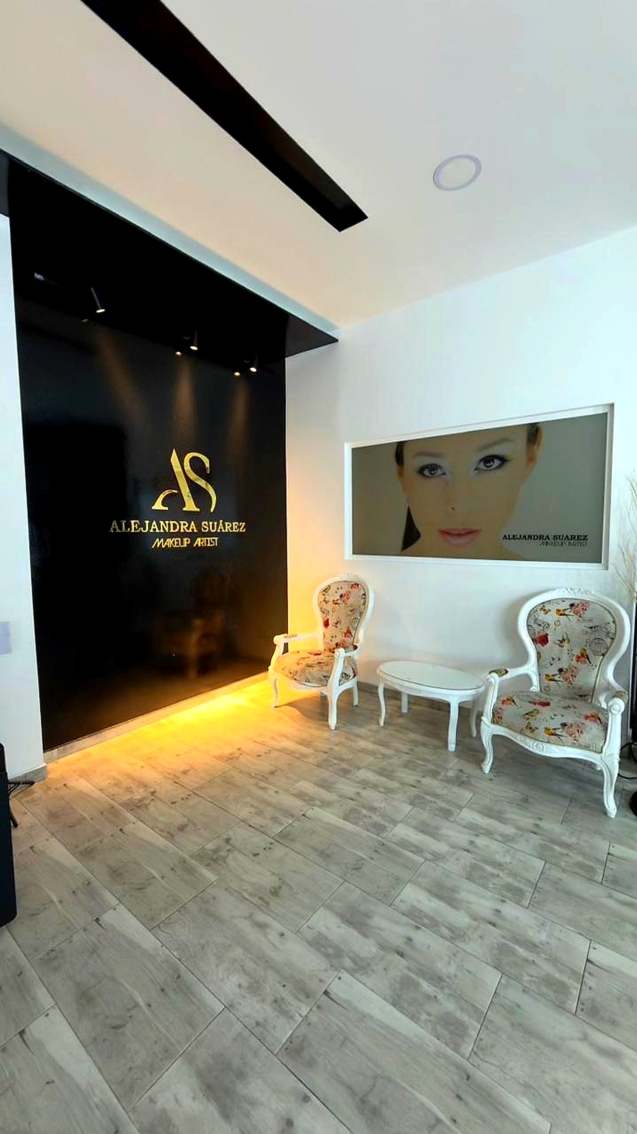 Lobby de Alejandra Suárez Makeup Artist con logo dorado AS en pared y sala de espera con sillones